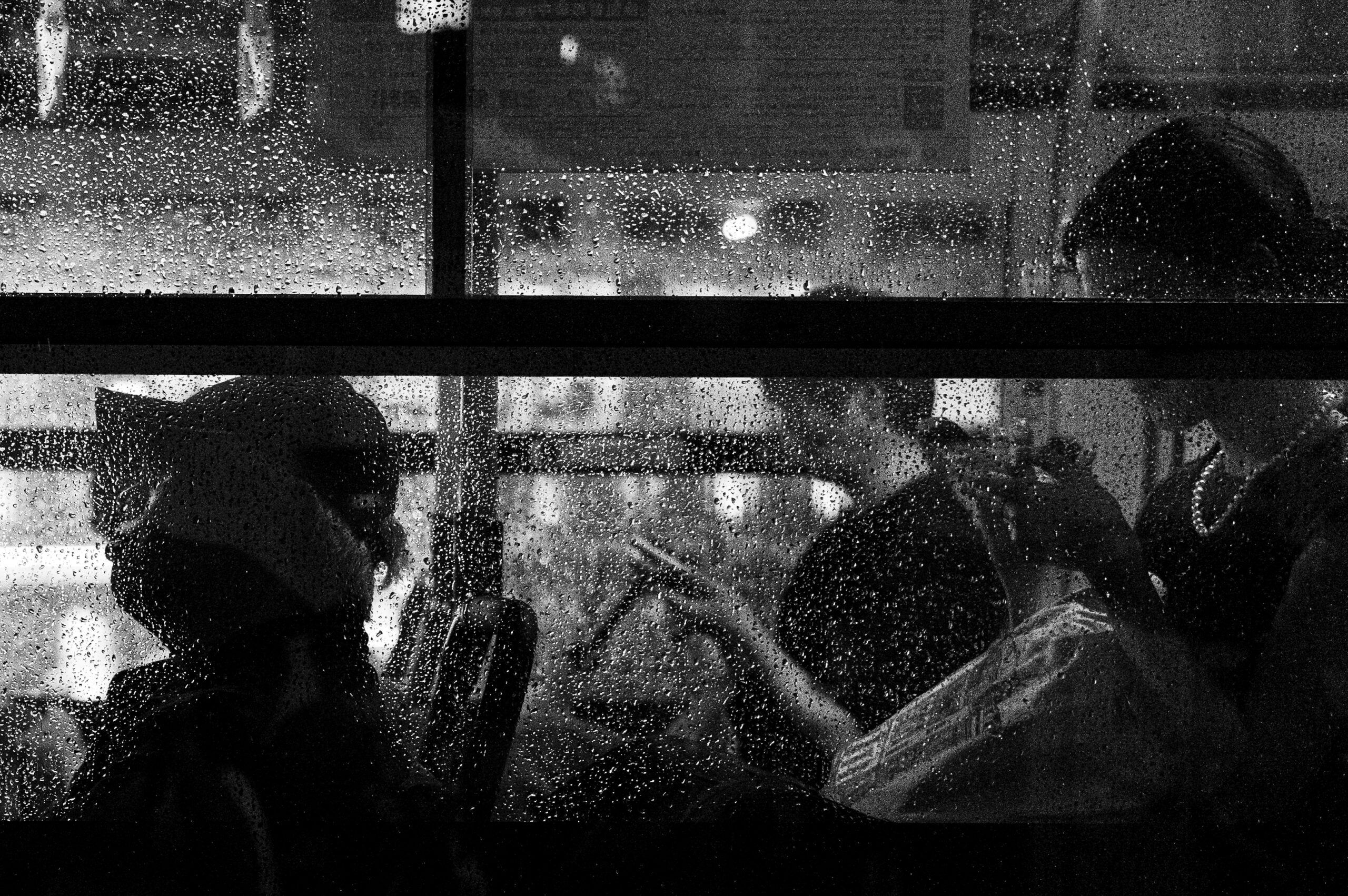 雨粒のついた窓越しに見える乗客たちのモノクロ写真