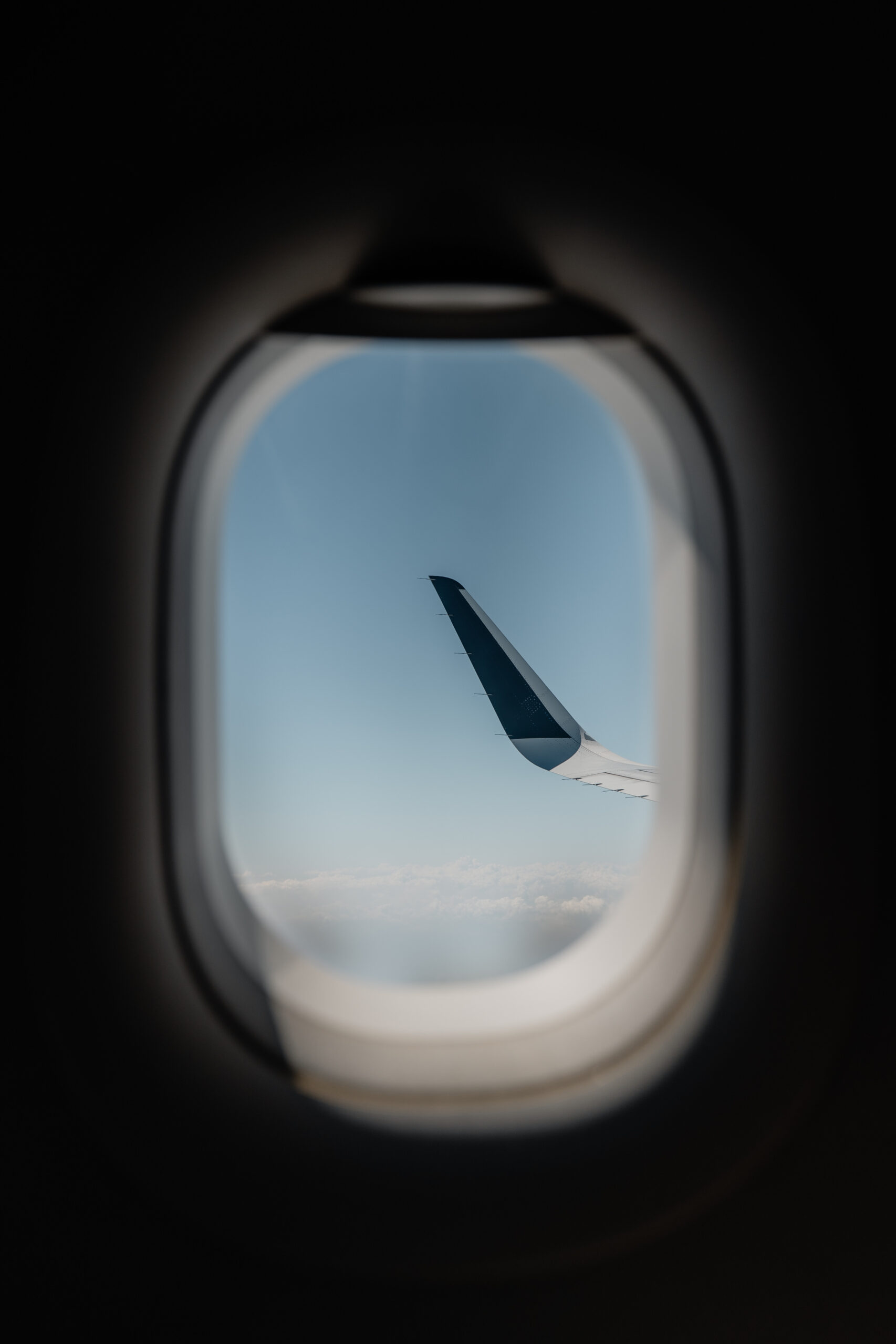 飛行機の窓越しに見える翼と青空と雲